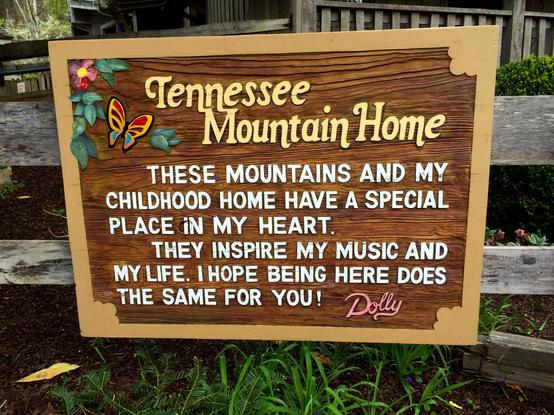 Background: Green trees and bushes...
Middleground: Wooden building with a partial porch...
Foreground: Wooden sign with a butterfly and flower in the top left corner on a wooden fence with greenery below it saying: "Tennessee Mountain Home... These mountains and my childhood home have a special place in my heart. They inspire my music and my life. I hope being here does the same for you! Dolly..."

Created: 4/07/2016 4:42pm
Aperture: ƒ∕2.2
Exposure: 1∕398 s
ISO: 32
Focal Length: 4.15 mm