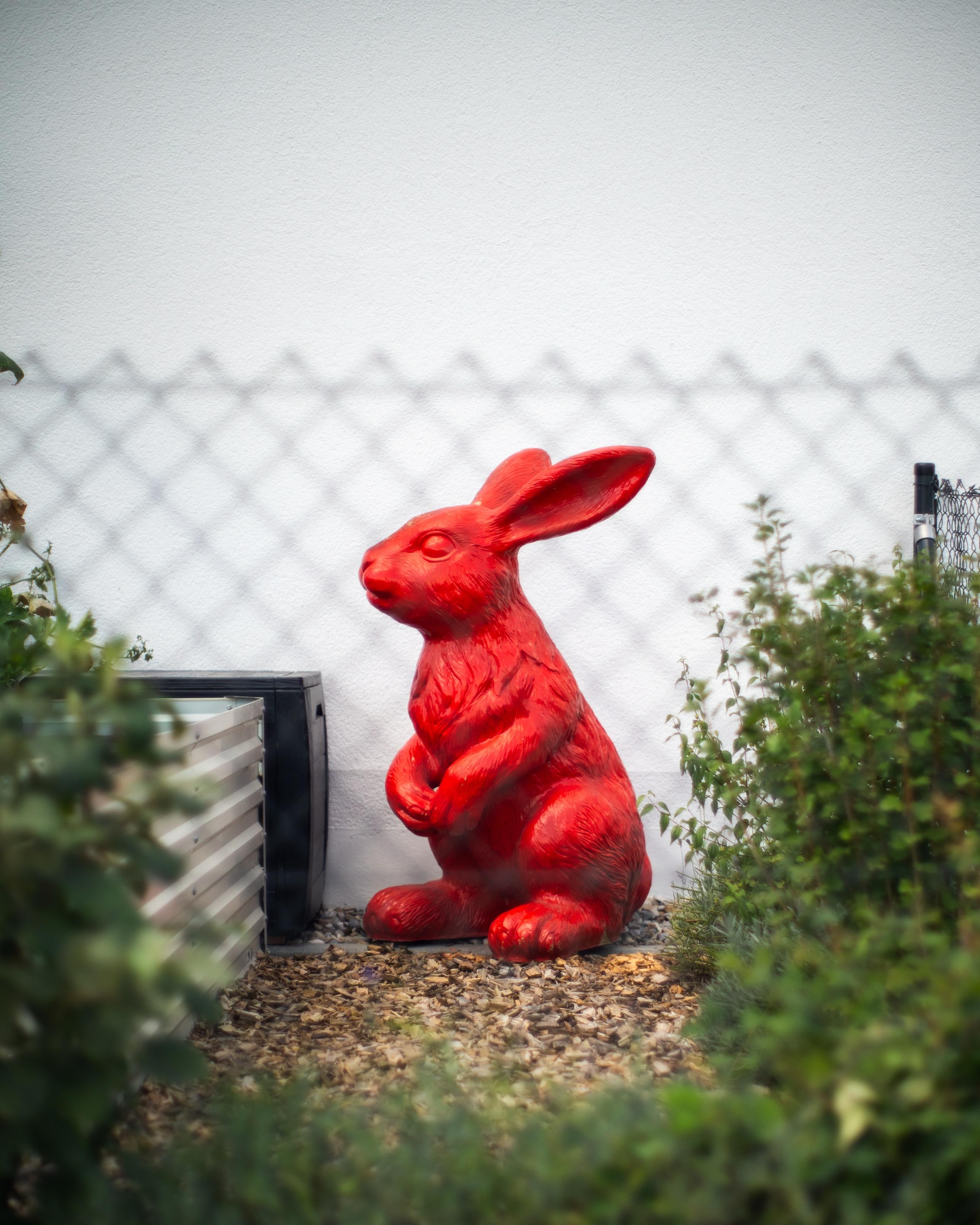Ein roter gut ein Meter hoher Plastikhase sitzt in einem Garten