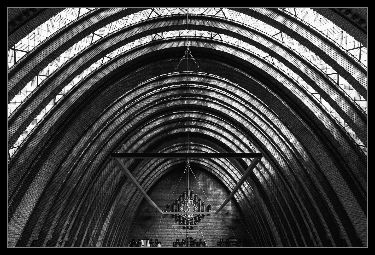 Blick in eine begenförmige Halle in der eine große Rechteckige Lampe hängt. Im Hintergrund ist eine Uhr zu erkennen.